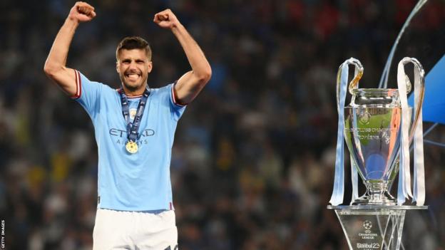 Manchester City midfielder Rodri celebrates in front of the Champions League trophy